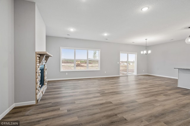 unfurnished living room featuring dark hardwood / wood-style floors, a stone fireplace, a chandelier, and a textured ceiling