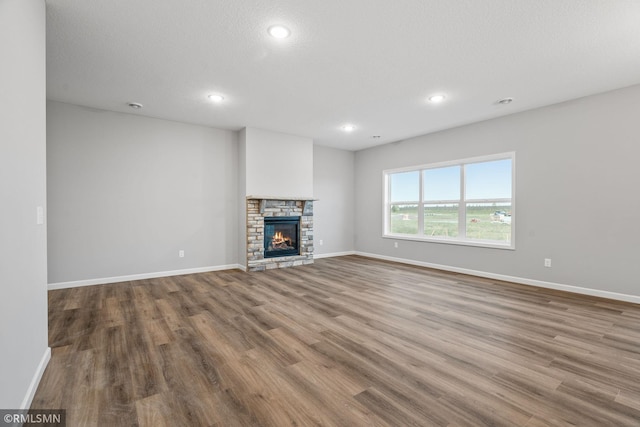 unfurnished living room with a textured ceiling, hardwood / wood-style floors, and a stone fireplace