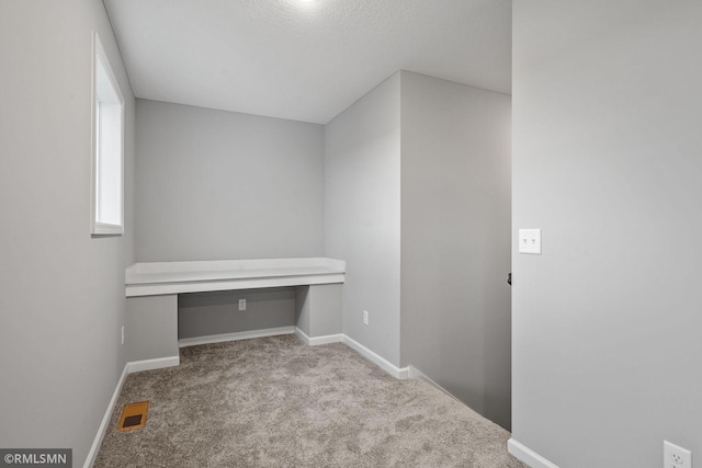 unfurnished office featuring built in desk and light colored carpet