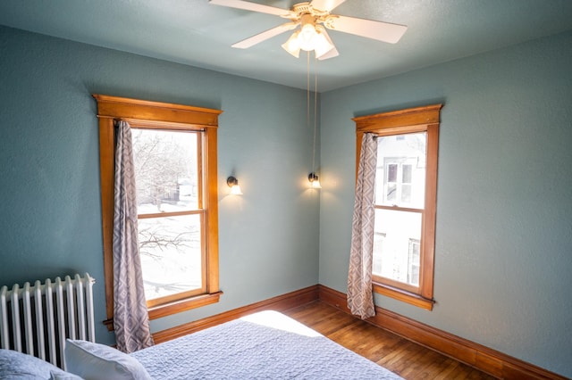 bedroom with hardwood / wood-style floors, ceiling fan, radiator, and multiple windows