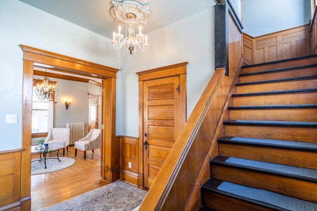 stairs with radiator heating unit, hardwood / wood-style floors, and an inviting chandelier