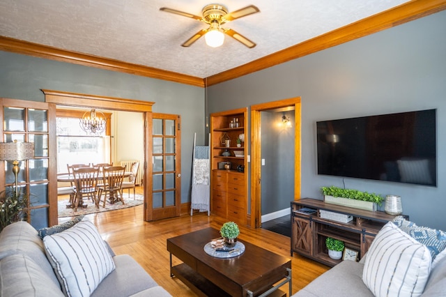 living room featuring a textured ceiling, light wood-type flooring, ceiling fan with notable chandelier, and ornamental molding