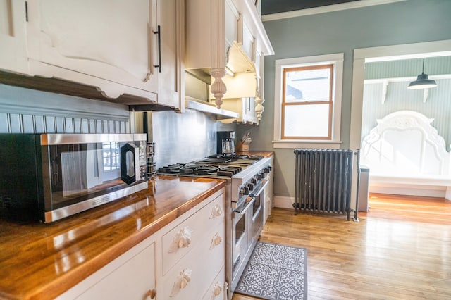 kitchen featuring butcher block counters, radiator heating unit, white cabinets, and appliances with stainless steel finishes