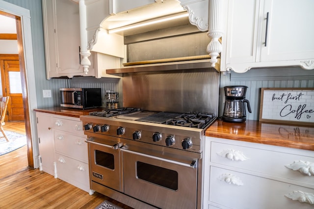 kitchen featuring ventilation hood, white cabinets, light wood-type flooring, butcher block countertops, and stainless steel appliances