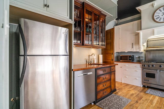 kitchen featuring appliances with stainless steel finishes, ornamental molding, sink, light hardwood / wood-style flooring, and white cabinets