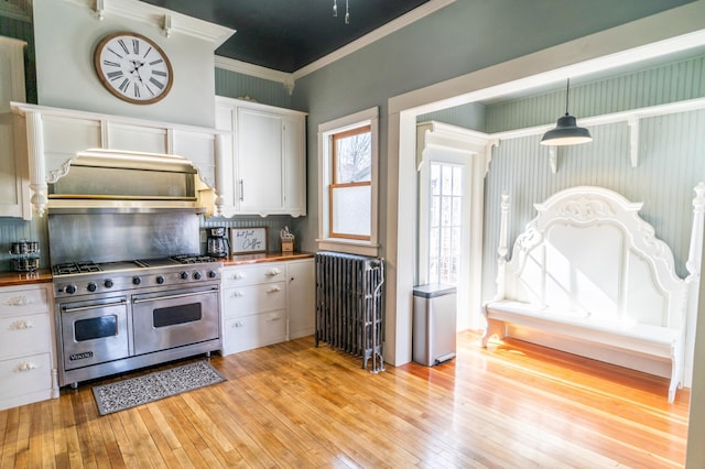 kitchen with pendant lighting, range with two ovens, radiator heating unit, light hardwood / wood-style floors, and white cabinetry