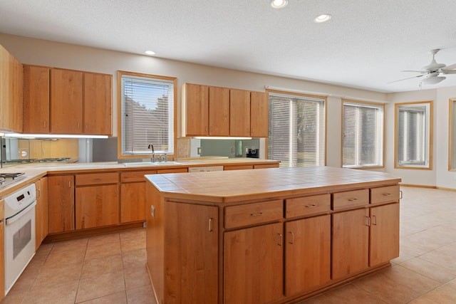 kitchen featuring a wealth of natural light, tile counters, sink, oven, and a kitchen island