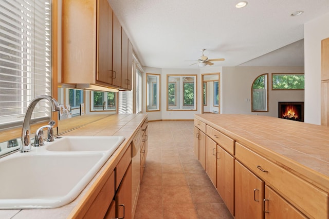 kitchen featuring tile countertops, dishwasher, sink, ceiling fan, and light tile patterned flooring