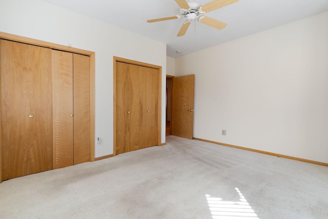 unfurnished bedroom featuring ceiling fan, light carpet, and multiple closets