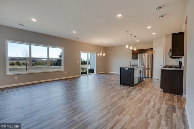 kitchen with a notable chandelier, light hardwood / wood-style floors, pendant lighting, appliances with stainless steel finishes, and an island with sink