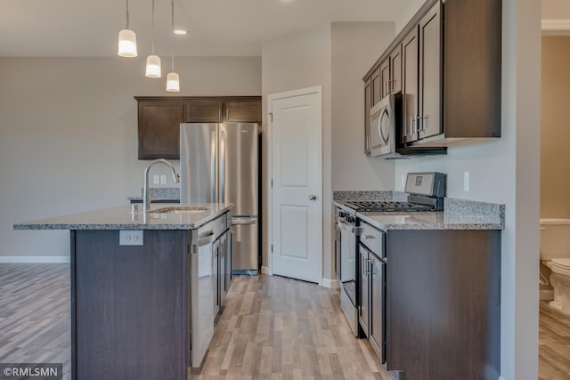 kitchen with appliances with stainless steel finishes, an island with sink, sink, hanging light fixtures, and light stone counters