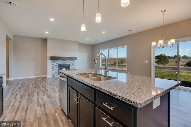 kitchen with light stone counters, sink, hanging light fixtures, and a center island with sink