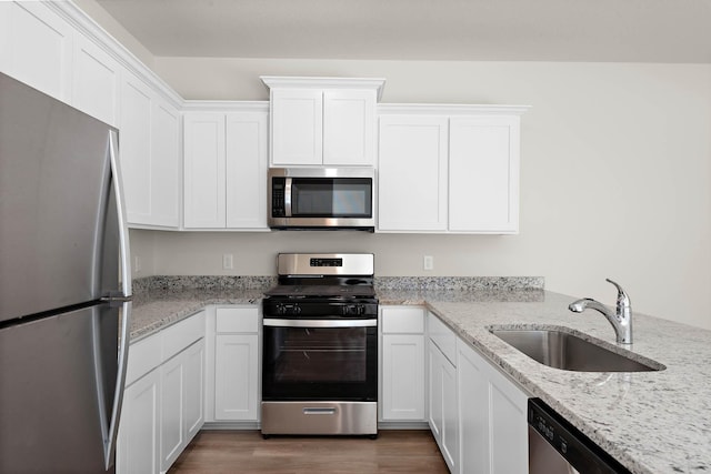 kitchen with sink, light stone countertops, appliances with stainless steel finishes, white cabinetry, and wood-type flooring