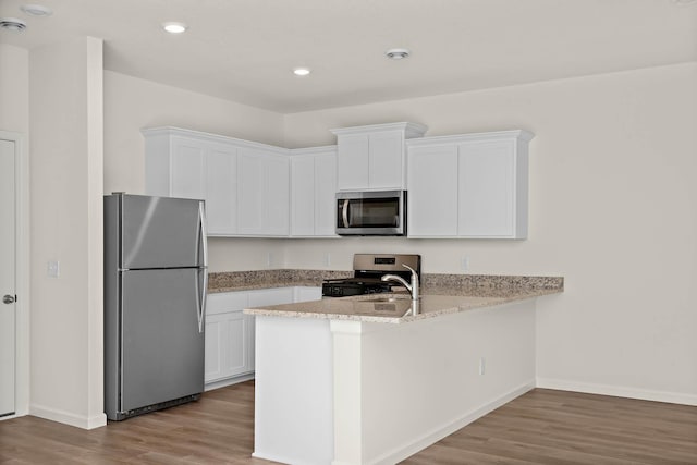 kitchen featuring light stone countertops, appliances with stainless steel finishes, kitchen peninsula, light hardwood / wood-style flooring, and white cabinetry