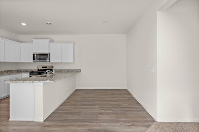 kitchen with light stone counters, kitchen peninsula, appliances with stainless steel finishes, white cabinets, and light wood-type flooring