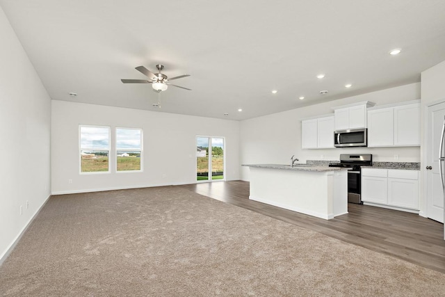 kitchen featuring ceiling fan, stainless steel appliances, light stone counters, a center island with sink, and white cabinets