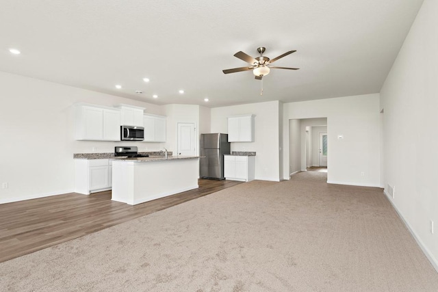 kitchen with ceiling fan, stainless steel appliances, dark colored carpet, a kitchen island with sink, and white cabinets