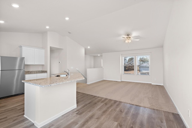 kitchen with white cabinets, sink, ceiling fan, light stone counters, and stainless steel refrigerator