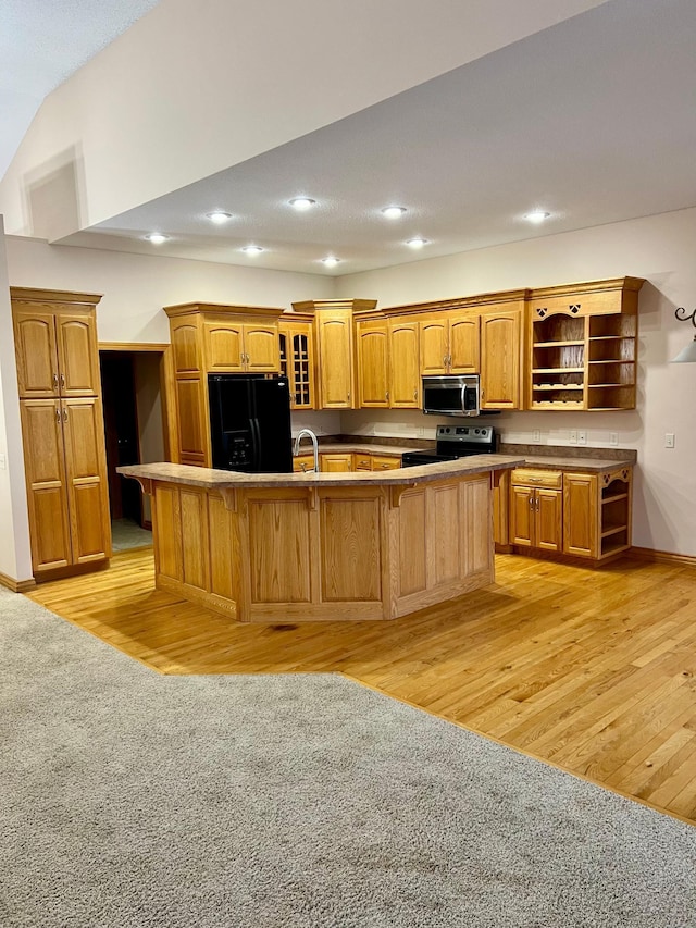 kitchen with an island with sink, a breakfast bar, black appliances, light wood-type flooring, and sink