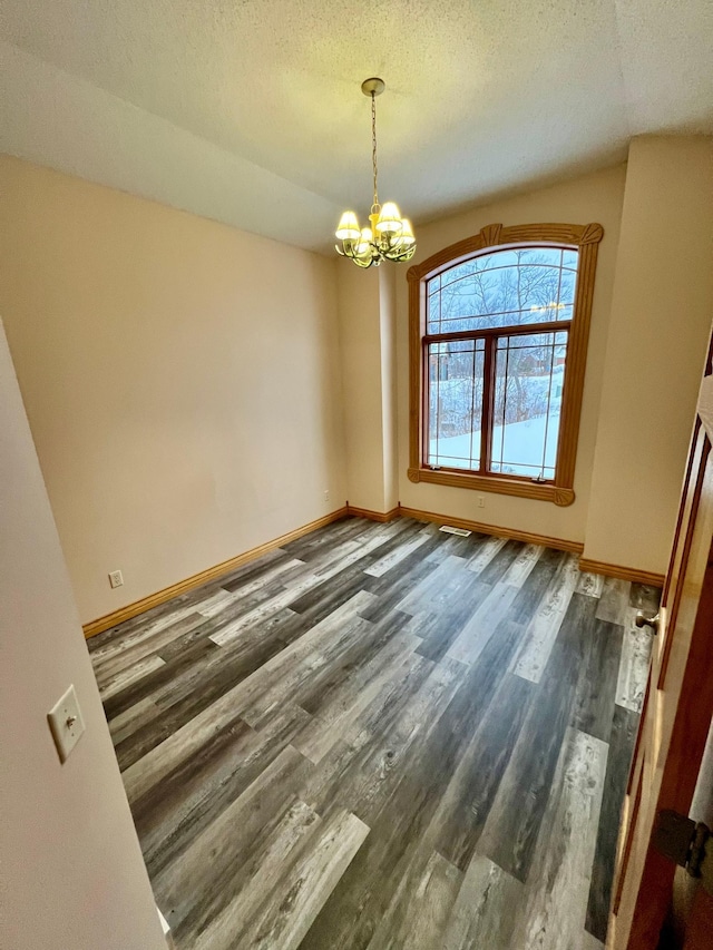 spare room with a notable chandelier, dark hardwood / wood-style flooring, and a textured ceiling