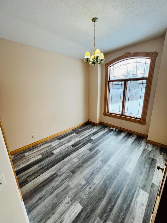 unfurnished dining area with a textured ceiling, a chandelier, and dark hardwood / wood-style floors