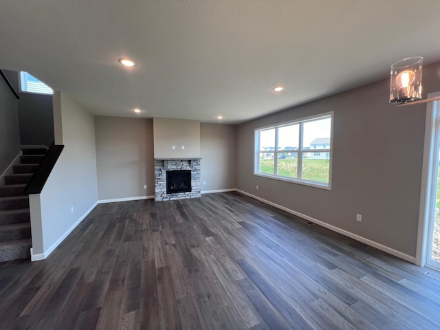 unfurnished living room featuring a stone fireplace and dark wood-type flooring