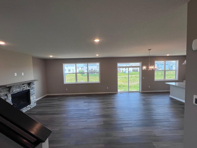 unfurnished living room with a chandelier, dark hardwood / wood-style flooring, and a stone fireplace