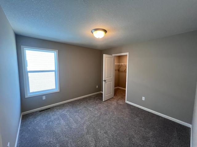 unfurnished bedroom with dark carpet, a spacious closet, a textured ceiling, and a closet