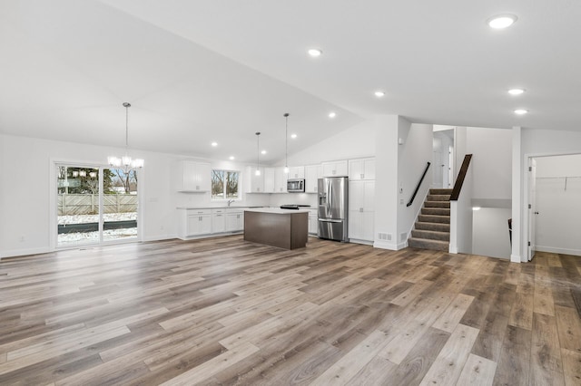 unfurnished living room with light wood-type flooring, high vaulted ceiling, and a notable chandelier