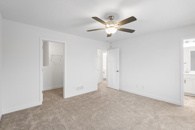 unfurnished bedroom featuring ensuite bath, ceiling fan, light colored carpet, a walk in closet, and a closet