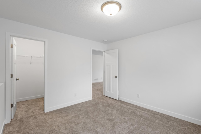 unfurnished bedroom with a textured ceiling, a spacious closet, light carpet, and a closet