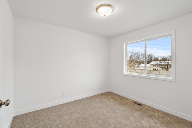 unfurnished room with a textured ceiling, carpet floors, visible vents, and baseboards