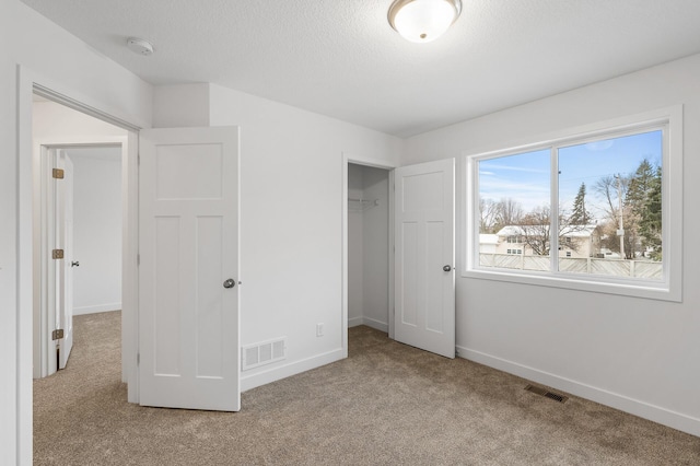 unfurnished bedroom featuring baseboards, a textured ceiling, visible vents, and carpet flooring