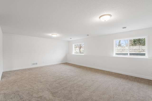 carpeted spare room with visible vents, a textured ceiling, and baseboards