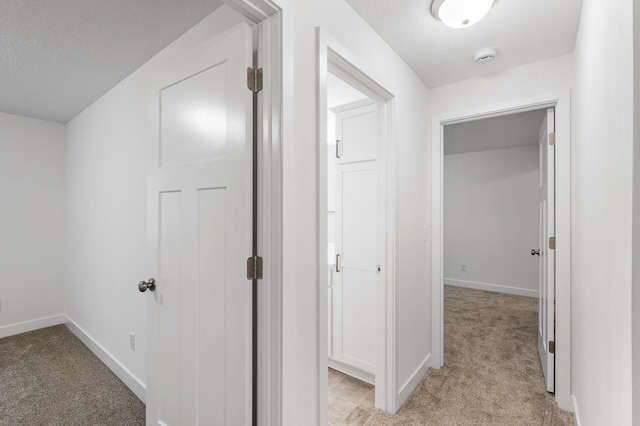 hallway featuring baseboards, a textured ceiling, and light colored carpet