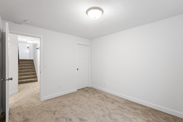 spare room with stairs, a textured ceiling, carpet flooring, and baseboards