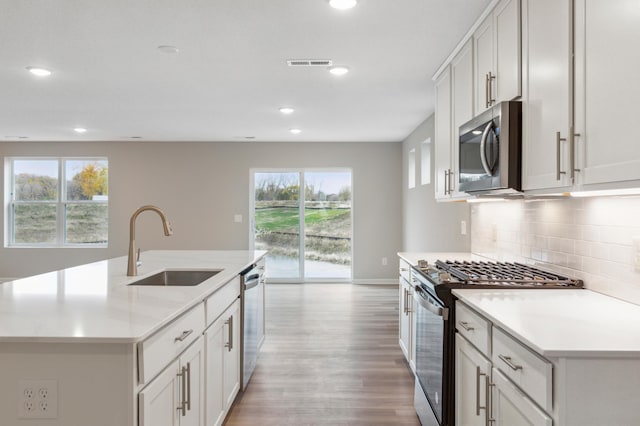 kitchen featuring white cabinetry, appliances with stainless steel finishes, decorative backsplash, a kitchen island with sink, and sink