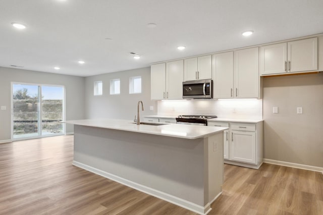 kitchen featuring white cabinetry, a center island with sink, appliances with stainless steel finishes, light hardwood / wood-style flooring, and sink