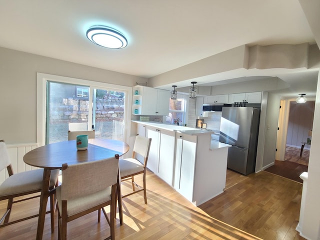 kitchen featuring wood-type flooring, white cabinetry, stainless steel appliances, hanging light fixtures, and kitchen peninsula