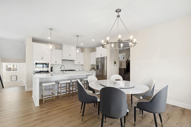 dining space with light wood-type flooring, an inviting chandelier, and sink