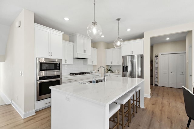 kitchen featuring white cabinetry, light stone countertops, stainless steel appliances, tasteful backsplash, and a center island with sink