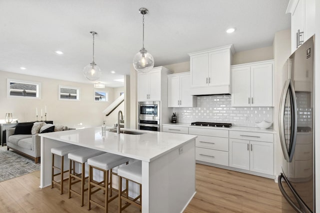 kitchen with a kitchen island with sink, pendant lighting, white cabinets, and stainless steel appliances