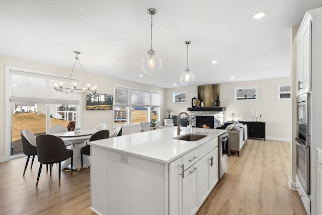 kitchen with white cabinets, decorative light fixtures, a stone fireplace, and sink