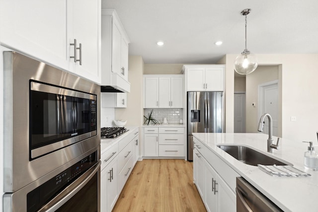 kitchen featuring light stone countertops, appliances with stainless steel finishes, backsplash, sink, and white cabinets