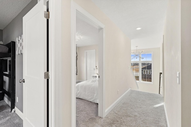 hall featuring a chandelier, a textured ceiling, and carpet floors