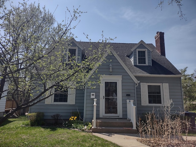 cape cod house featuring a front lawn, a chimney, and a shingled roof