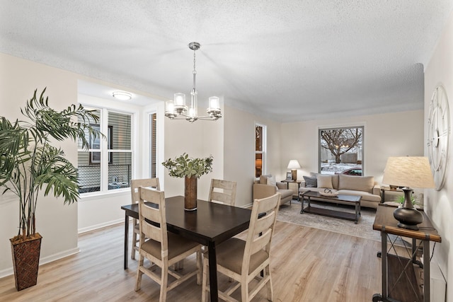 dining room featuring a textured ceiling, a notable chandelier, light wood-type flooring, and a wealth of natural light