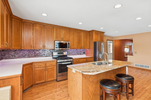 kitchen with a kitchen bar, sink, a kitchen island with sink, stainless steel appliances, and light hardwood / wood-style floors