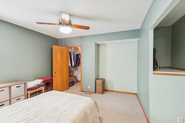 bedroom featuring ceiling fan, a textured ceiling, light carpet, a spacious closet, and a closet