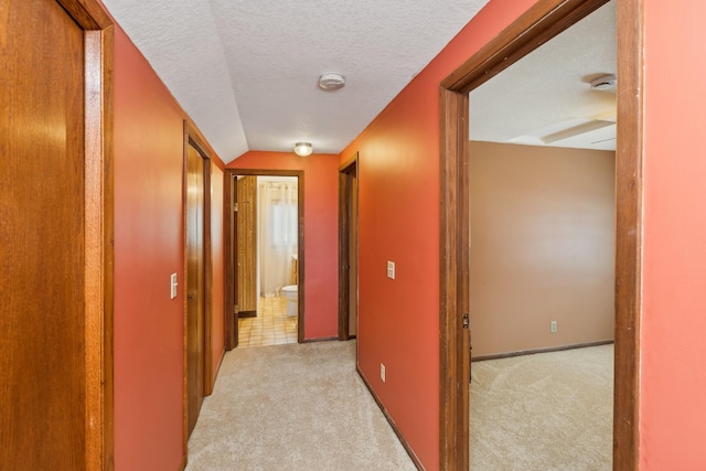 hall with vaulted ceiling, light carpet, and a textured ceiling